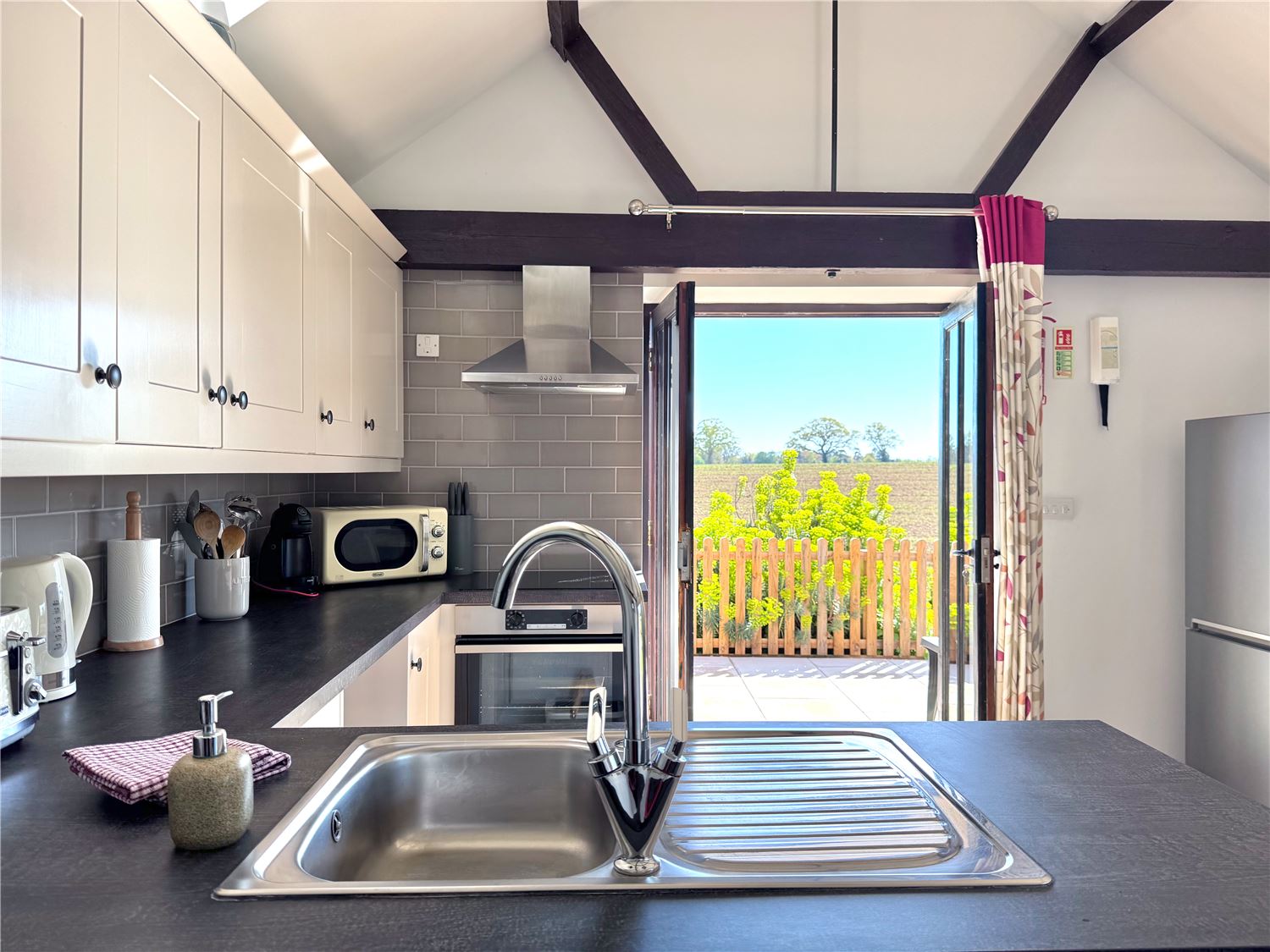Well equipped kitchen opening onto enclosed patio with countryside view at holiday accommodation in Norfolk